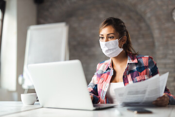 Fototapeta na wymiar Young businesswoman wears mask while working at casual office