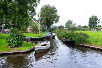 Metal and wooden boats that are standing moored in the channel, visible trees and buildings.