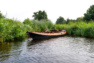 Naklejka na ściany i meble An abandoned wooden boat standing in the canal between the reeds.