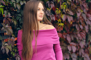 young beautiful woman in a pink knitted sweater looks to the side, against the background of wild...