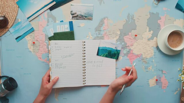 Horizontal from above zoom-in flat lay footage of woman putting tick in checklist doing travelling preparations before flight