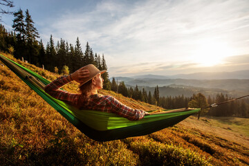 Woman hiker resting after climbing in a hammock at sunset
