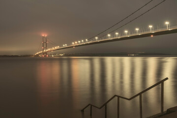 Humber bridger with lights and reflections and estuary at daybreak. Hessle, UK.