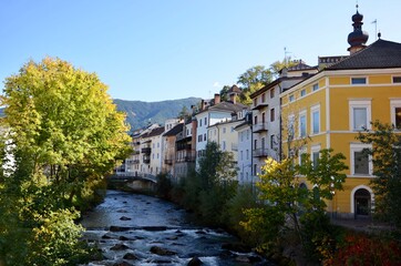 Fototapeta na wymiar Historic buildings in the old town of Bruneck (Brunico) in the valley Pustertal in South Tirol, river Ahr in the middle, autumn landscape, a sunny day, blue sky background