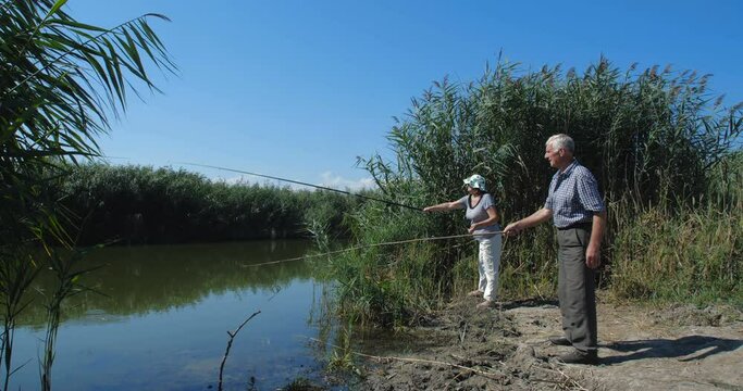 Active happy and healthy elderly European couple in casual clothes  fishing with a rods near the lake on a warm summer day with their two granddaughters. slow motion 4k 50 fps