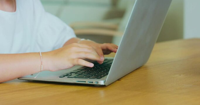 Closeup hands of teen girl, with bracelets on wrists, writing on laptop. Laptop is on the table.