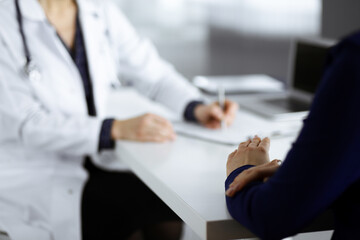 Unknown woman-doctor is writing some medical recommendations to her patient, while they are sitting together at the desk in the cabinet in a clinic. Physician is using a clipboard, close-up. Perfect
