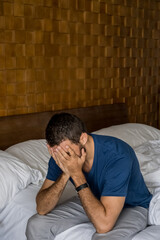 Fototapeta premium Stressed, depressed or grieving man sitting on bed covering face with hands and crying. Worried and frustrated male suffering depression or life crisis feeling desperate and helpless