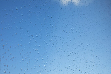Clear blue sky view through a window with rain drops on the glass.