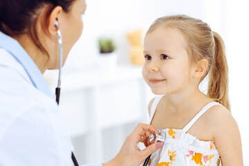 Doctor examining a little girl by stethoscope. Happy smiling child patient at usual medical inspection. Medicine and healthcare concepts