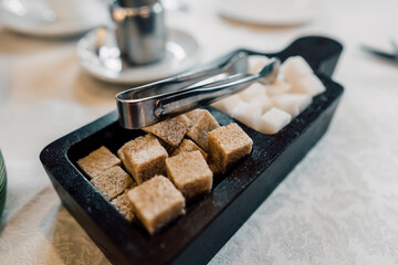 Bowl with pieces of white and brown sugar cubes and with sugar-tongs.