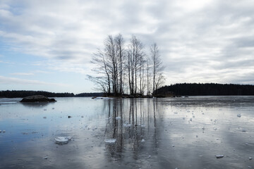 Frozen lake with ice and island with trees. Winter season. Cloudy day. Cold weather in Finland.