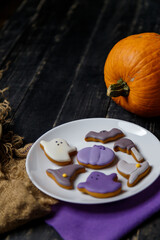 Pumpkin and Halloween cookies on white plate, sackcloth on black wooden background. Hallooween trick or treat concept. Copy space. Vertical shot.
