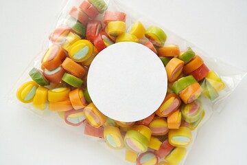 Blank white round sticker mockup on birthday or baby shower party favor bag with colorful candies,...