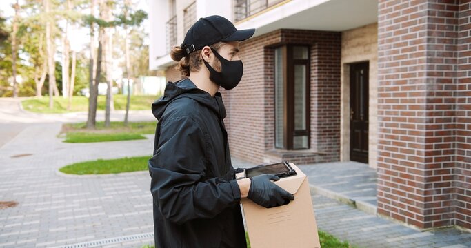Caucasian male courier in medical mask delivering carton parcel to female client to home.