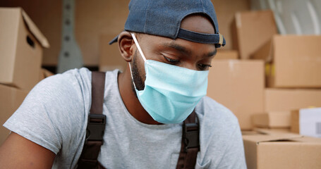 Portrait of African American delivery man in mask in front of his van.