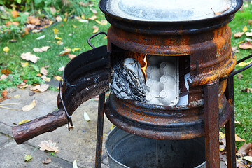 Burning garbage in a garden oven. Handmade metal garden outdoor heater with fire. Cardboard and...