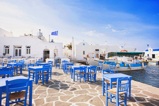 Fototapeta Outdoor restaurant in Greece. Traditional greek cafe with beautiful street at the background. Food, travel and vacation concept. Naousa, greek fishing village on Paros island, Cyclades, Greece