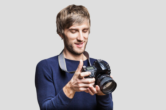 Young cheerful man photographer takes images with digital camera studio shot isolated on white background. Travel, photography, professional freelance work, hobby and active lifestyle concept