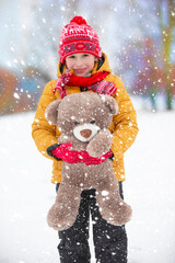 Child in winter. The boy plays in the street with a soft toy.