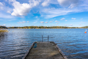 Fototapeta na wymiar Old wooden pier or jetty for yachts and boats. Autumn landscape of the coast of Sweden. Forest islands with colorful trees in the gulf of the Baltic Sea. Panoramic view of Scandinavia in an autumn.
