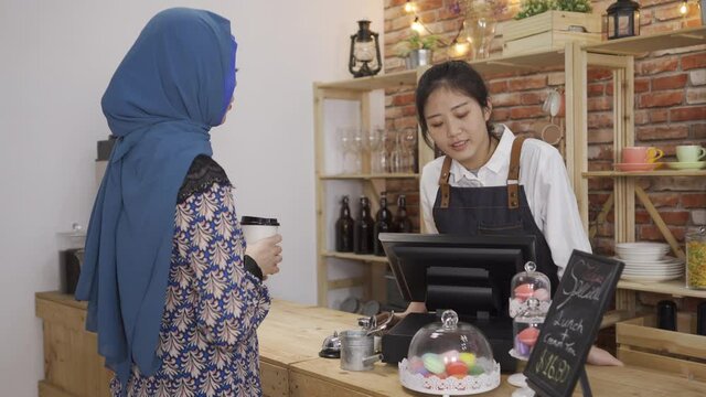 asian korean barista girl showing and introducing their daily sweet dessert to muslim woman customer on counter table in cafe bar.