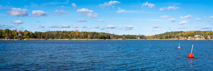 Autumn landscape of the coast of Sweden. Forest islands with colorful trees in the gulf of the Baltic Sea. Panoramic view of Scandinavia in an autumn. Bright red buoys float on the surface of water.
