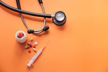top view of stethoscope, pills and syringe on orange background 