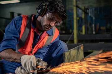 A male engineer is grinding steel in an industrial factory.