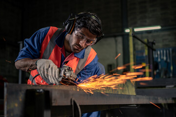 A male engineer is grinding steel in an industrial factory.