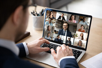Close up rear view businessman engaged in online conference, using laptop, sitting at desk, diverse...