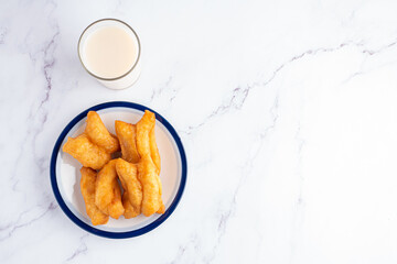 Deep-fried dough sticks on white plate and a glass of soybean milk on marble table