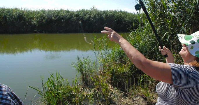 Active happy and healthy elderly European couple in casual clothes  fishing with a rods near the lake on a warm summer day with their two granddaughters. slow motion 4k 50 fps