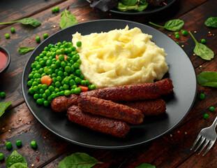 Vegetarian vegan sausages with mashed potato and green peas in black plate