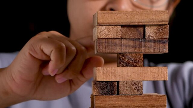 Woman thinking and concentrating on pulling out a wooden blocks in room alone. Jenga falls on the table. Concept of success and failure in the business.