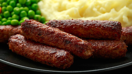Vegetarian vegan sausages with mashed potato and green peas in black plate