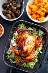 Top view of a whole roasted chicken served with fresh salad in black pan. Thanksgiving or family dinner celebration cooking concept.