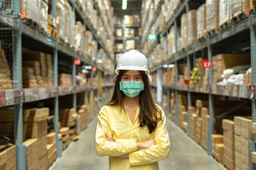 Fototapeta premium Female warehouse worker inspecting a warehouse in a factory. Wear a safety helmet and mask for working safety. Concept of warehouse.