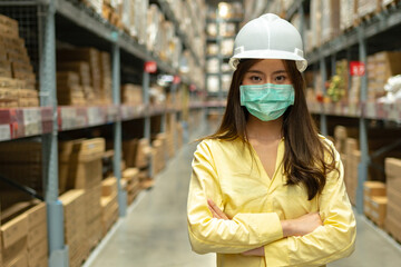 Fototapeta premium Female warehouse worker inspecting a warehouse in a factory. Wear a safety helmet and mask for working safety. Concept of warehouse.
