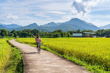 Young happy woman enjoying and riding a bicycle in paddy field while traveling at Pua, Thailand