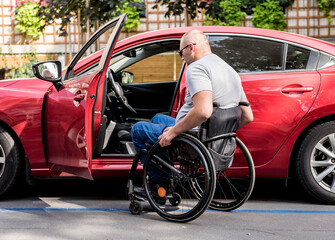 Young handicapped driver getting in red car fom wheelchair