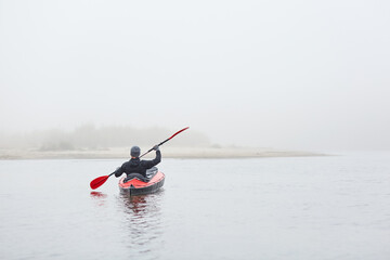 Fototapeta na wymiar Kayaker rowing boat to bank of river, holding paddle in hands. wearing warm clothing, sportsman posing backwards in canoe, water sport, extreme.