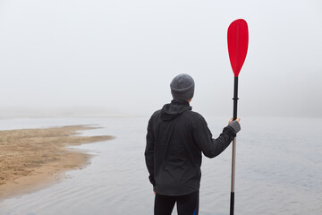 Back view of kayaking on river bank with paddle in hands, looking in distance, enjoying beautiful...