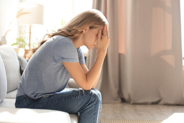 Sad woman sitting on a sofa in the living room.