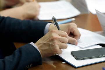 In the frame, a man's hand with a fountain pen writes in a notebook. Dressed in a business suit