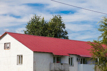 The roof of an old wooden house covered with sheets of brown metal tiles on a background of green coniferous trees on a summer day. Business selling building materials or helping low-income families.