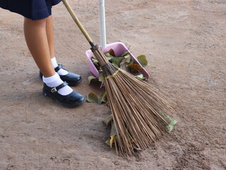 Female students sweeping the leaves on the concrete floor.