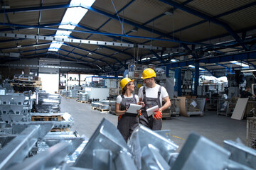 Factory workers in industrial production hall sharing ideas.