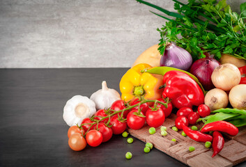 Food background on black wood table. Ingredients for cooking food - cherry tomatoes, onions, potatoes, red and yellow peppers, peas in the pod and garlic. copy space.