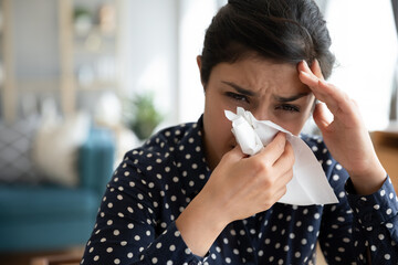 Close up image sick indian woman feels unwell blowing her nose into paper napkin reducing breathing...